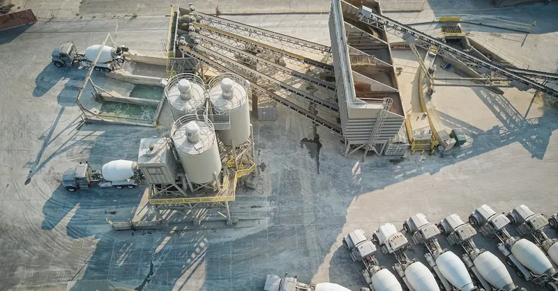 A drone-captured aerial view of an industrial concrete mixing plant with trucks and machinery.