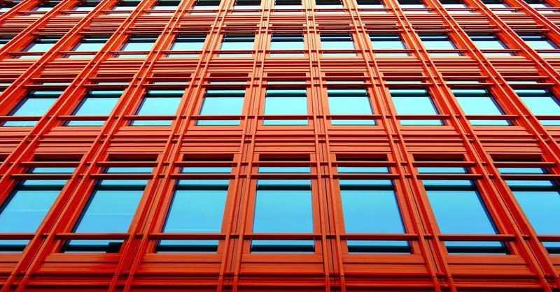 Low angle shot of a modern red building with glass windows reflecting the sky.
