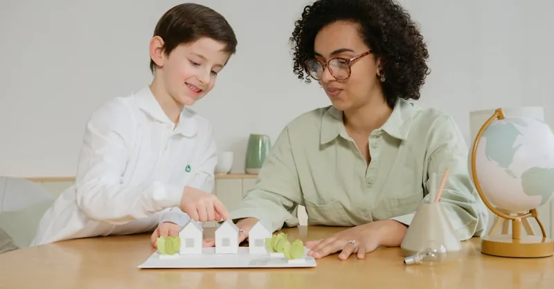 A young boy and a teacher exploring sustainable energy models with model houses and a globe in a classroom setting.