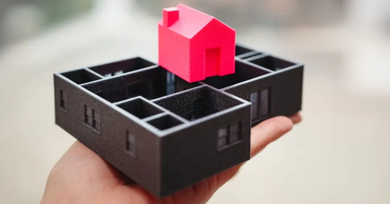 A hand holding a 3D printed model of a house and floor plan, showcasing architectural design.