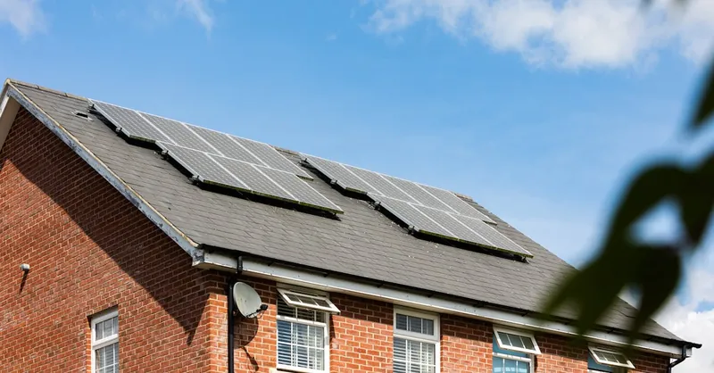 Brick house featuring solar panels on the roof under a clear blue sky, promoting sustainable energy.