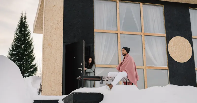 Contemporary house in a snowy setting with two people enjoying a winter day.