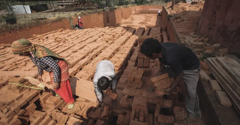 Workers handling bricks in an outdoor factory setting, illustrating manual labor in manufacturing.