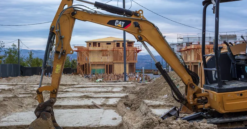 Excavator working on a new residential construction site with wooden frames.
