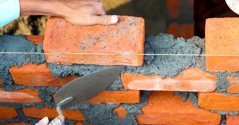 Hands laying bricks with cement in a construction setting, showcasing precise masonry work.