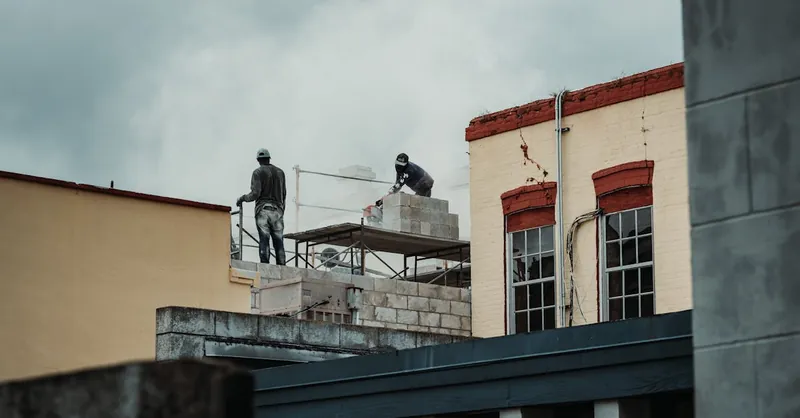 Urban construction scene with workers laying bricks on a building site, captured during the day.