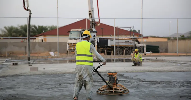 Workers smoothing concrete on a construction site with heavy machinery equipment.