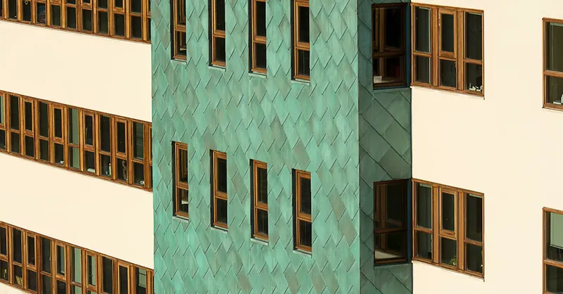 Close-up view of a modern building facade featuring teal panels and wooden framed windows.