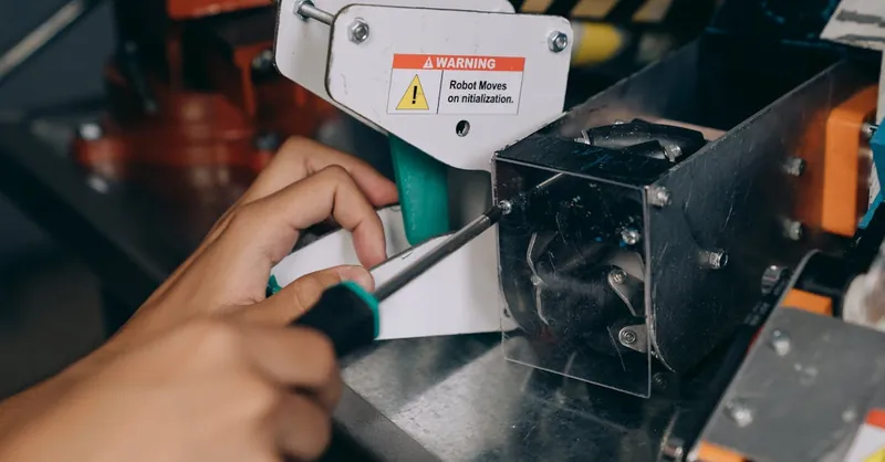Close-up of a hand using a screwdriver to fix industrial robot machinery indoors.