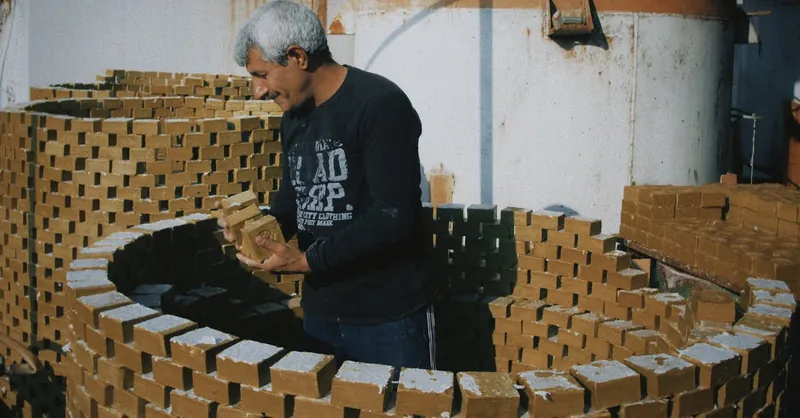 Worker stacking bricks in an industrial area during daylight hours, focusing on construction process.