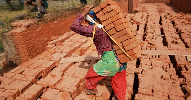 A worker carries stacked bricks at a construction site, showcasing hard labor and industrious effort.