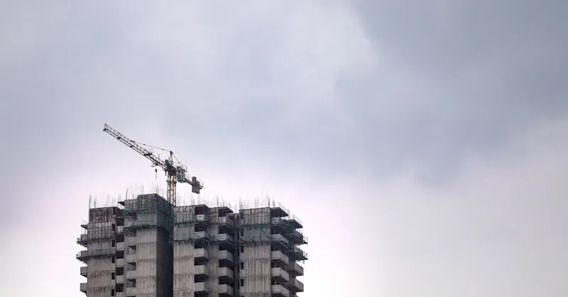 High-rise building construction site with crane against a cloudy sky, showcasing urban development.