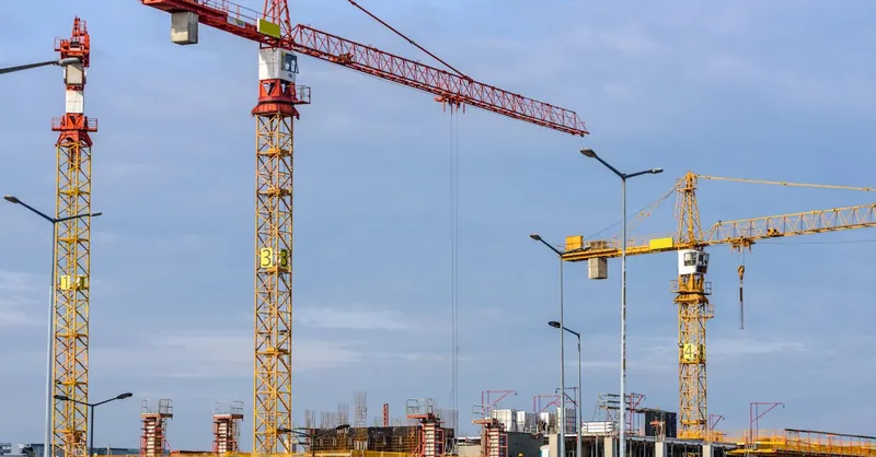 Multiple tower cranes working on a large construction site with blue sky backdrop.