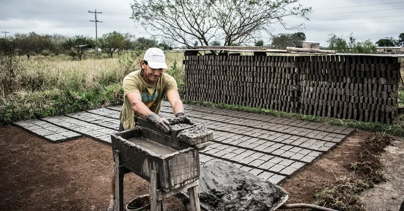 Man shaping cement bricks outdoors, showcasing traditional construction work.